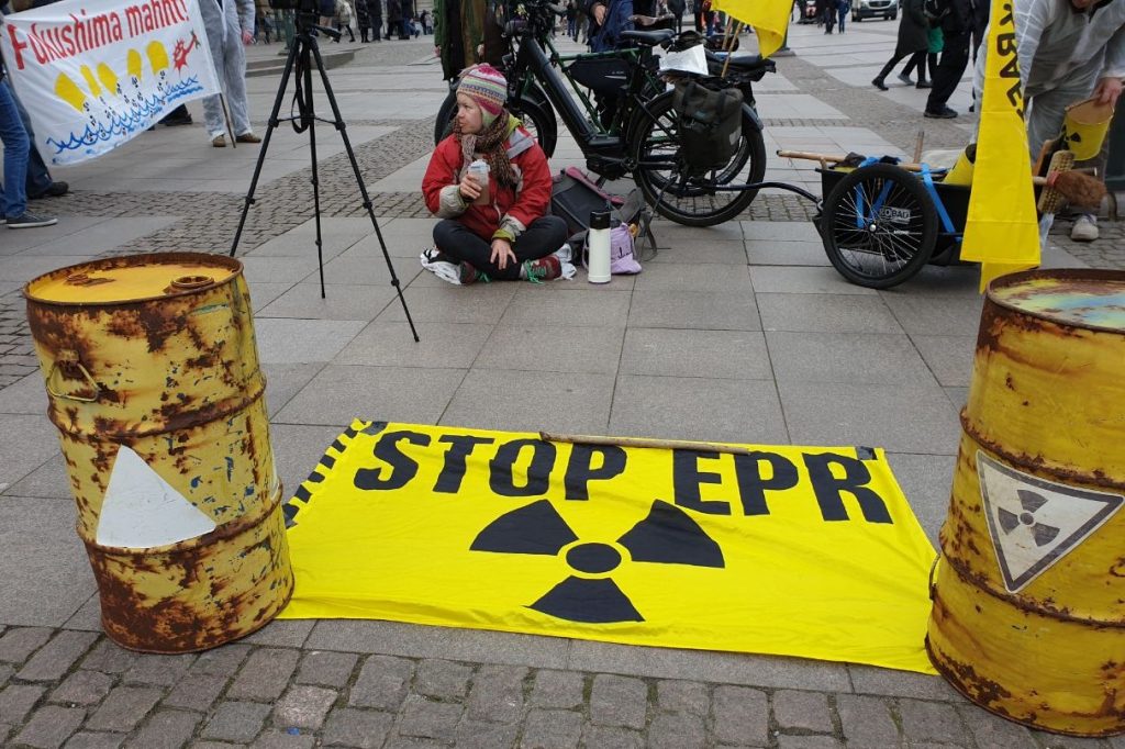 Banner stopp EPR Atomreaktor zwichen 2 gelben Fässen.