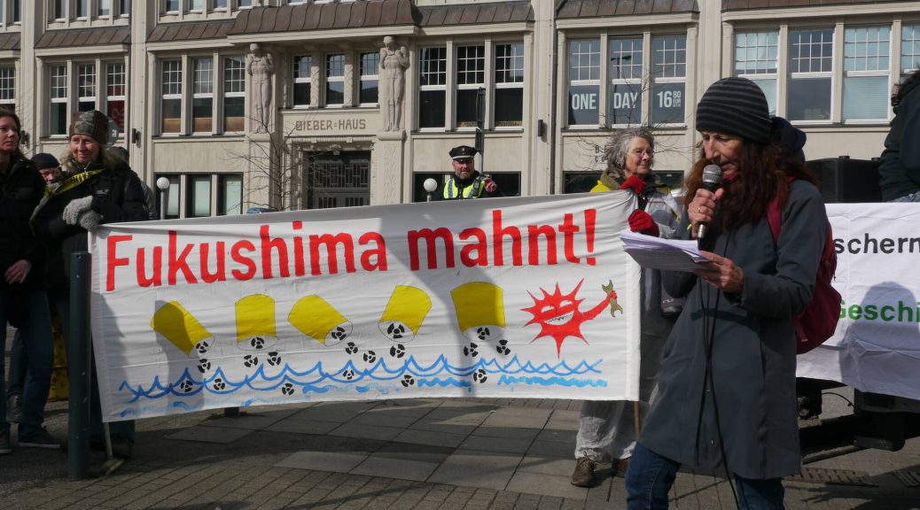 eine Person spricht ins Mikrofon mit Banner Fukushima Mahnt im Hintergrund