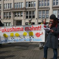 eine Person spricht ins Mikrofon mit Banner Fukushima Mahnt im Hintergrund